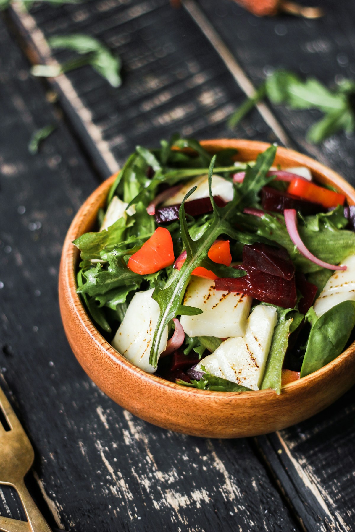 A colourful garden salad in a wooden bowl, photographed from above on dark wood